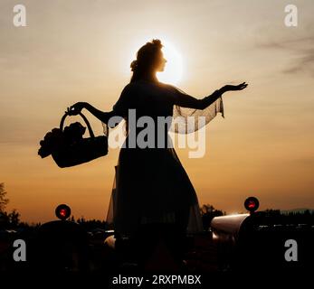 Silhouette of woman standing against setting sun with basket in hand Stock Photo