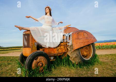 Woman doing split on top of tractor standing in vast tulip field Stock Photo