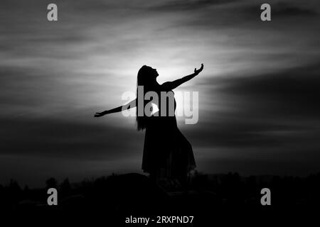 Silhouette of long-haired woman standing against setting sun Stock Photo