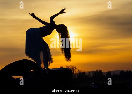 Silhouette of long-haired woman posing against setting sun Stock Photo