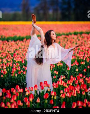 Long-haired brunette bending over backwards in vast tulip field Stock Photo