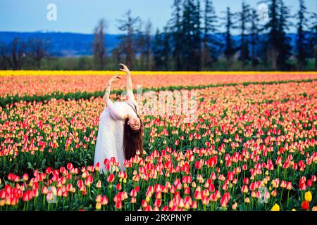 Long-haired brunette bending over backwards in vast tulip field Stock Photo
