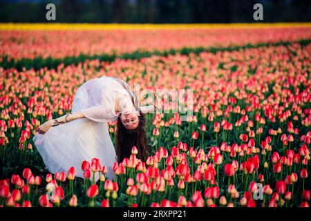 Long-haired brunette bending over backwards in vast tulip field Stock Photo