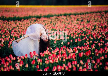 Long-haired brunette bending over backwards in vast tulip field Stock Photo