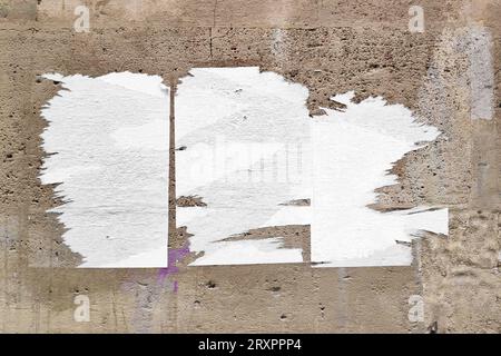 Full-frame weathered limestone wall with three torn blank posters. Stock Photo