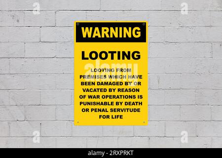 Yellow warning sign screwed to a brick wall to warn about the consequences if caught looting. Stock Photo