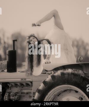 Woman holding colorful umbrella doing split on top of rusty tractor Stock Photo