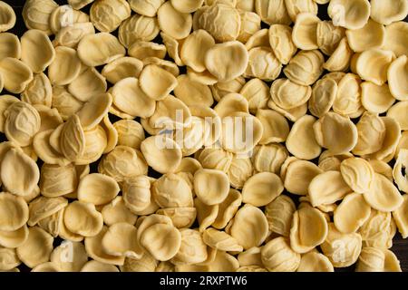 Dried Yellow orecchiette Pasta Scatttered on a Wooden Table: Pieces of uncooked orecchiette pasta on a dark wood background Stock Photo