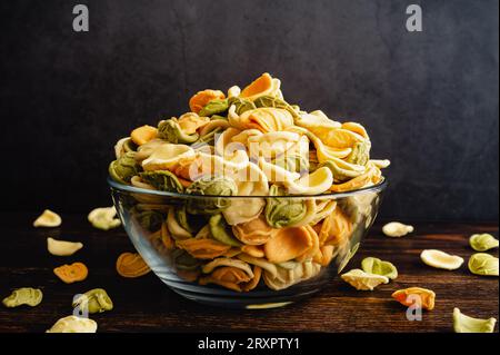 Dried Tricolor Orecchiette Pasta in a Glass Bowl Viewed in Profile: A bowl of uncooked orecchiette pasta in a glass bowl viewed from the side Stock Photo