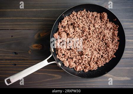 Browned Ground Beef in a Large Skillet: Cooked ground beef in a large non-stick frying pan on a wooden table Stock Photo