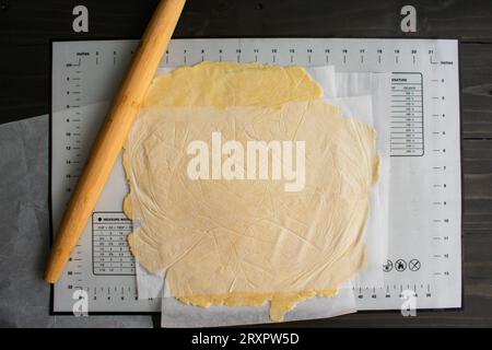 Rolling Out Pie Dough Between Sheets of Parchment Paper: Pie dough rolled out with a bamboo French rolling pin on a silicone mat Stock Photo