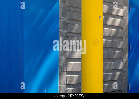 Closeup blue and yellow urban scene; sunlit blue wall, yellow pole, grey bricks in Vancouver, Canada Stock Photo