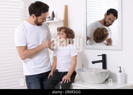 Father helping his son to brush teeth in bathroom Stock Photo