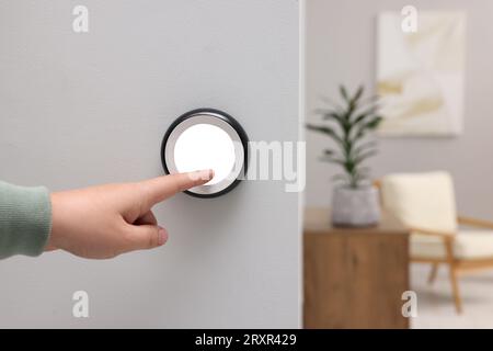 Man adjusting thermostat on white wall indoors, closeup. Smart home system Stock Photo