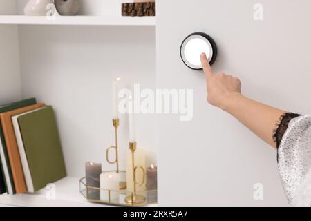 Woman adjusting thermostat on white wall indoors, closeup. Smart home system Stock Photo