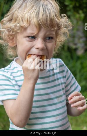 A little boy bites into a pastry Stock Photo