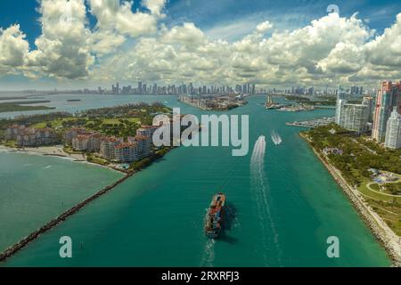 Commercial container ship entering Miami port harbor through main channel near South Beach. Luxurious hotels and residential buildings on waterfront Stock Photo