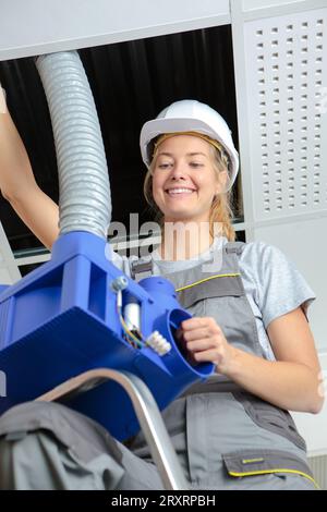 happy female worker fitting ventilation system in buildings ceiling Stock Photo