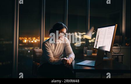 business woman engaging in a late-night virtual meeting on her laptop. Female remote worker sitting in her home office, discussing business projects v Stock Photo