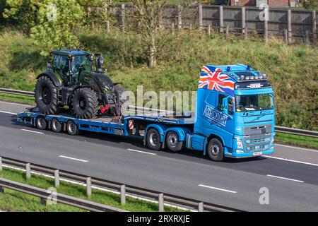 Ashcourt Group UK Blue Volvo FH carrying New Fendt Tractor on low-loader. heavy bulk Haulage delivery trucks, haulage, lorry, transportation, truck, cargo,  delivery, transport industry, supply chain freight, travelling at speed on the M6 motorway in Greater Manchester, UK Stock Photo