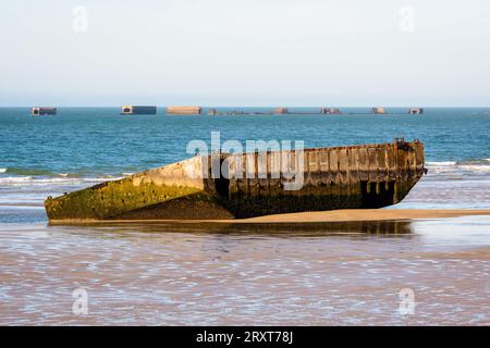 An element of the WWII Mulberry harbor built on Gold Beach in Arromanches, France, lying on the sand with remains of Phoenix caissons in the distance. Stock Photo