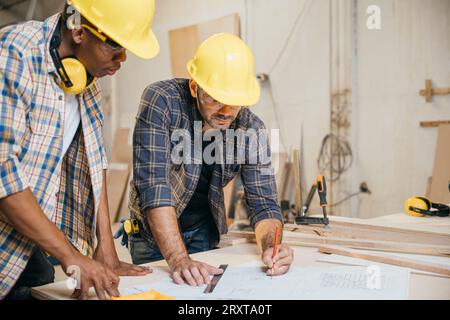 Two carpenter man wear helmet meeting planning job together at carpentry workshop Stock Photo