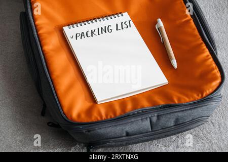 Travel Packing List For Vacation. Travel Packing Checklist For Holiday Or Business Trip. Open notepad with handwritten text Packing list in orange Stock Photo