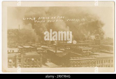 This black-and-white photographic postcard titled, Little Africa On Fire (Tulsa Race Riot June 1st. 1921) depicts a scene from the race riot. It appears to have been taken from an elevated location since most of what you can see are the roofs of buildings, most likely industrial, since many have large smoke stacks and a large amount of black smoke in the sky. Stock Photo