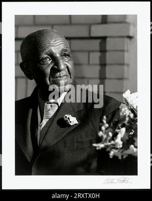 Photograph by Arthur RothsteinA black-and-white photograph of George Washington Carver, shown bust-length, wearing a suit and boutineer. An arrangement of flowers is in the lower right corner of the image, and there is a brick wall behind him. Stock Photo