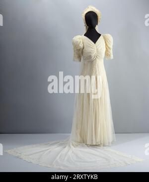 Wedding dress and accompanying accessories worn by Lollaretta Pemberton on her wedding day in 1939. The wedding gown is made of off-white lace and tulle. The gown is floor length and has lace puffed sleeves to the elbows.  There is ruching down the front of the front of the bodice. There is a matching long lace and tulle veil, with an attachable headpiece and faux floral headband. Stock Photo