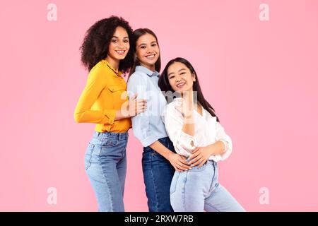 Diverse female friendship. Happy multiracial ladies embracing and posing, smiling at camera over pink studio background Stock Photo
