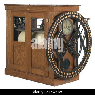 A large rectangular worker's time clock used by the R. H. Boyd Publishing Company. The front of clock has a large metal wheel with small black encircled numbers. Behind the large metal wheel is a clock featuring roman numerals and an AM/PM dial. Black type on the clock reads, ¿INTERNATIONAL / TIME RECORDING CO. / OF NEW YORK / ENDICOTT, N.Y.¿  The time clock has two doors with glass windows on both sides that show the inner workings of the clock. The inside of the clock has a large paper roll that works as a time sheet. Above the roll of paper in the front of the clock the days of the week are Stock Photo