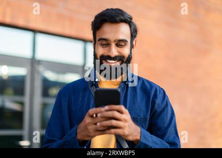 Portrait Of Smiling Bearded Arabian Man Using Smartphone Application Outdoor Stock Photo