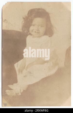 1930s SMILING GIRL SITTING IN CHAIR READING BOOK LOOKING AT CAMERA ...
