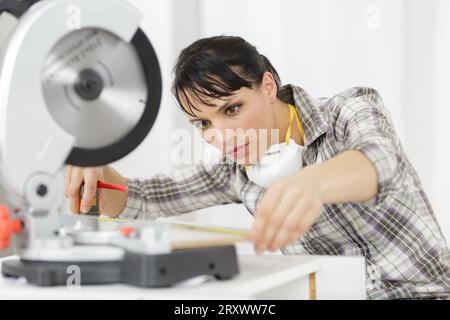 female mechanic measuring wood to be cut with circular saw Stock Photo