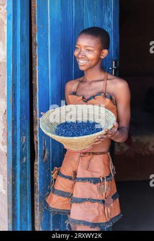 teenage african girl, village in Botswana holding a waved basket in front of the house, leather traditional costume Stock Photo