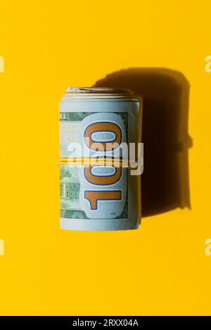 Wad of 100 USD dollar banknote bills on a yellow background, Roll of American dollar banknote bills on a yellow background Stock Photo