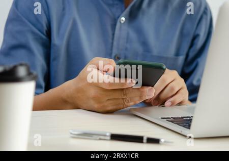 Man holding mobile smartphone on table with computer laptop. Stock Photo