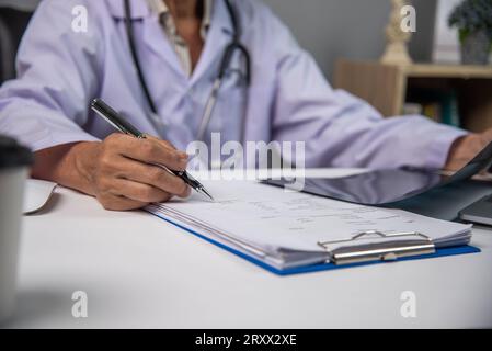 Female doctor holding a pen writing patient medical papers on clipboard and looking at x-ray film Stock Photo