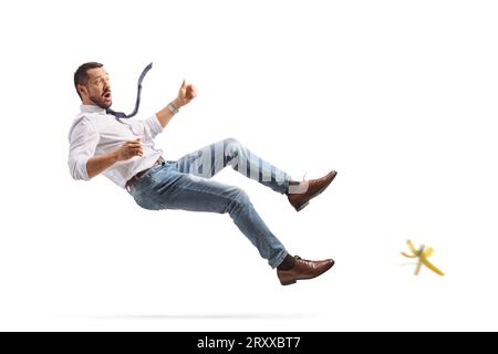 Full length profile shot of a young man falling on a banana skin isolated on white background Stock Photo