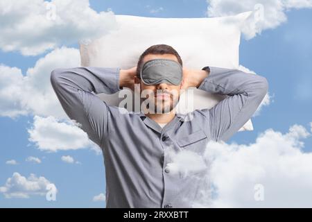 Man in pajamas with a sleeping mask laying on a pillow between clouds in the sky Stock Photo