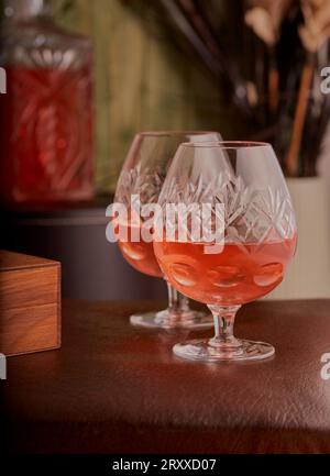 Pair of luxury brandy glasses with brandy inside them and a brandy decanter in the background. Stock Photo
