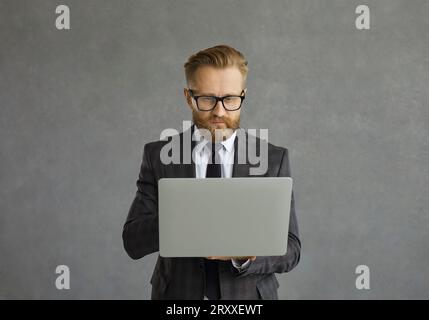 Focused serious businessman in suit and glasses working on modern laptop computer Stock Photo