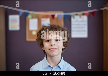 Front view portrait of cute curly haired boy looking at camera in preschool class, copy space Stock Photo