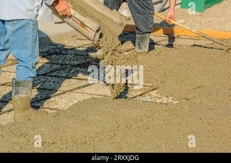 Workers pouring a slurry of concrete over a bed of gravel and rebar at a construction site Stock Photo