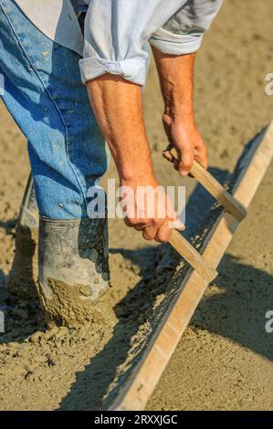 A worker using a wooden tool to screed a slurry of concrete at a construction site Stock Photo