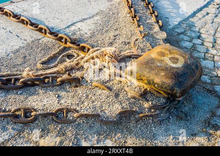 Old and rust mooring bollard with ropes and chains Stock Photo