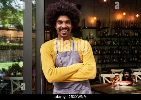 Young entrepreneur African man standing front of the camera and crossing arms at bar smiling. Stock Photo