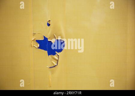 Landscape format colour photograph of peeling yellow paint revealing a deep blue coat underneath. Stock Photo