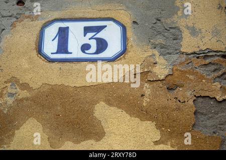 The number 13, on a white panel with blue surround against a yellow ochre painted wall, shot close up filling the frame. Stock Photo